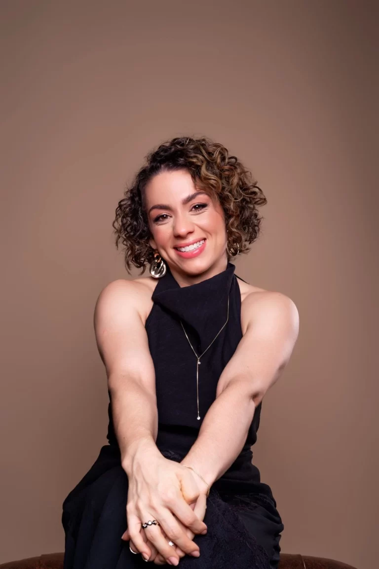 Dra. Kennya Henriqueta sorrindo, sentada, de blusa preta
